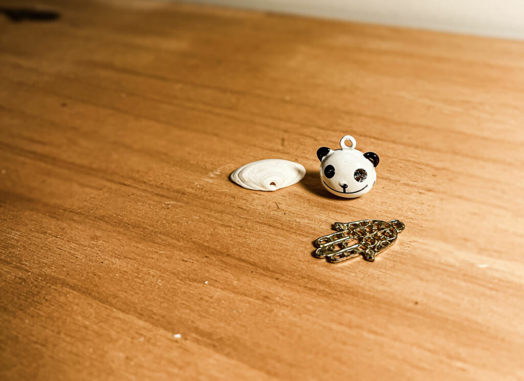 One is a panda’s head — a tiny bell inside it. One is a Fatma hand, a charm of protection. One is a seashell with a perfect hole.